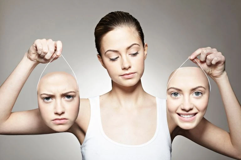 Foto de mujer con dos máscaras en sus manos con una expresión de enojo en una y la otra con expresión de alegría. Simboliza la bipolaridad.