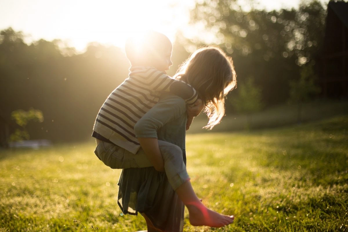 Juego libre y conexión con la naturaleza en la infancia Niños jugando al aire libre con sol, transmitiendo unión y alegría.