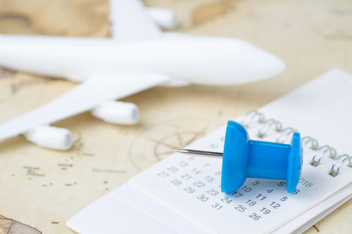 Chincheta azul marcando una fecha en un calendario junto a un avión de juguete, simbolizando la planificación de compras seguras para viajes.