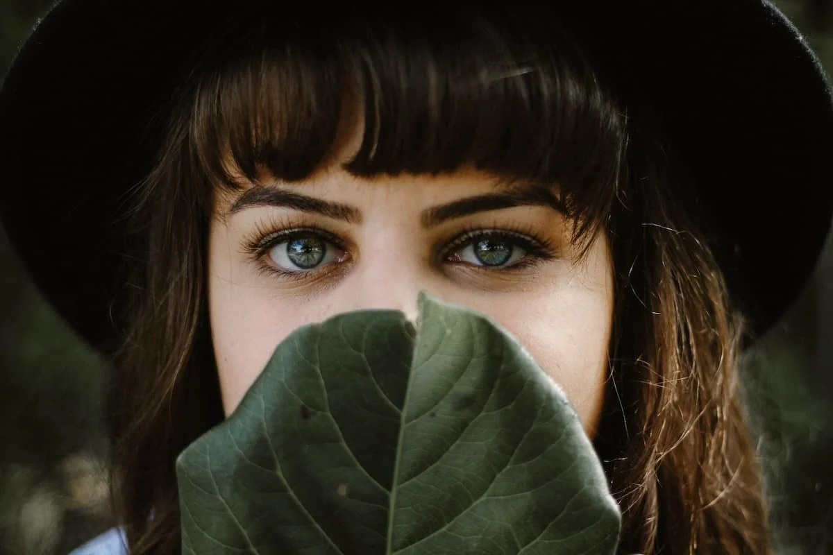 Primer plano de mujer cubriendo parte del rostro con una hoja, mostrando mirada atenta a su cabello
