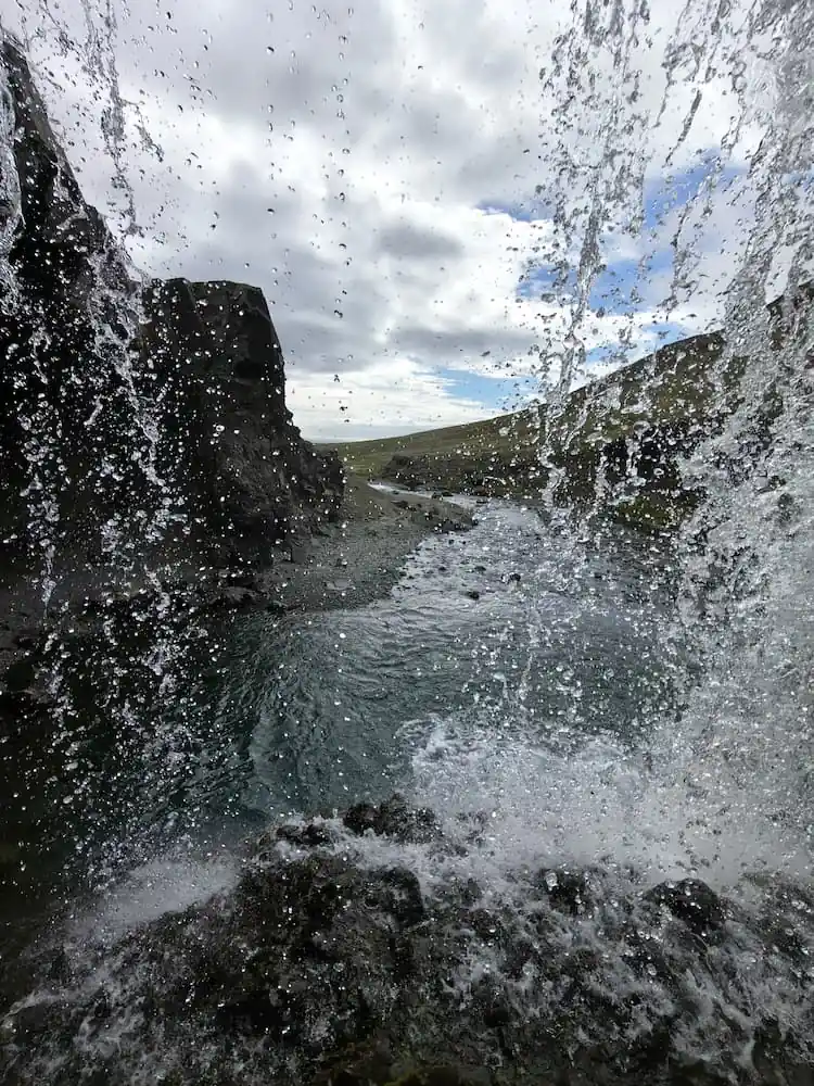 Vista desde detrás de una cascada capturada con un teléfono móvil, mostrando el movimiento del agua y el paisaje natural.