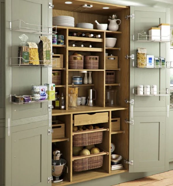 Alacena organizada en una cocina pequeña con estantes de madera, cestas de mimbre y frascos de alimentos.