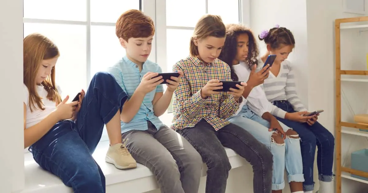 Niños sentados mirando el celular cada uno en su teléfono mostrando el uso excesivo de pantallas en la infancia