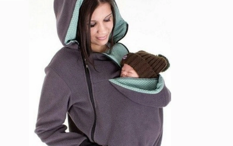 Mamá vistiendo una sudadera de porteo gris, diseñada para cubrir y abrigar a su bebé mientras duerme cómodamente en un portabebés.