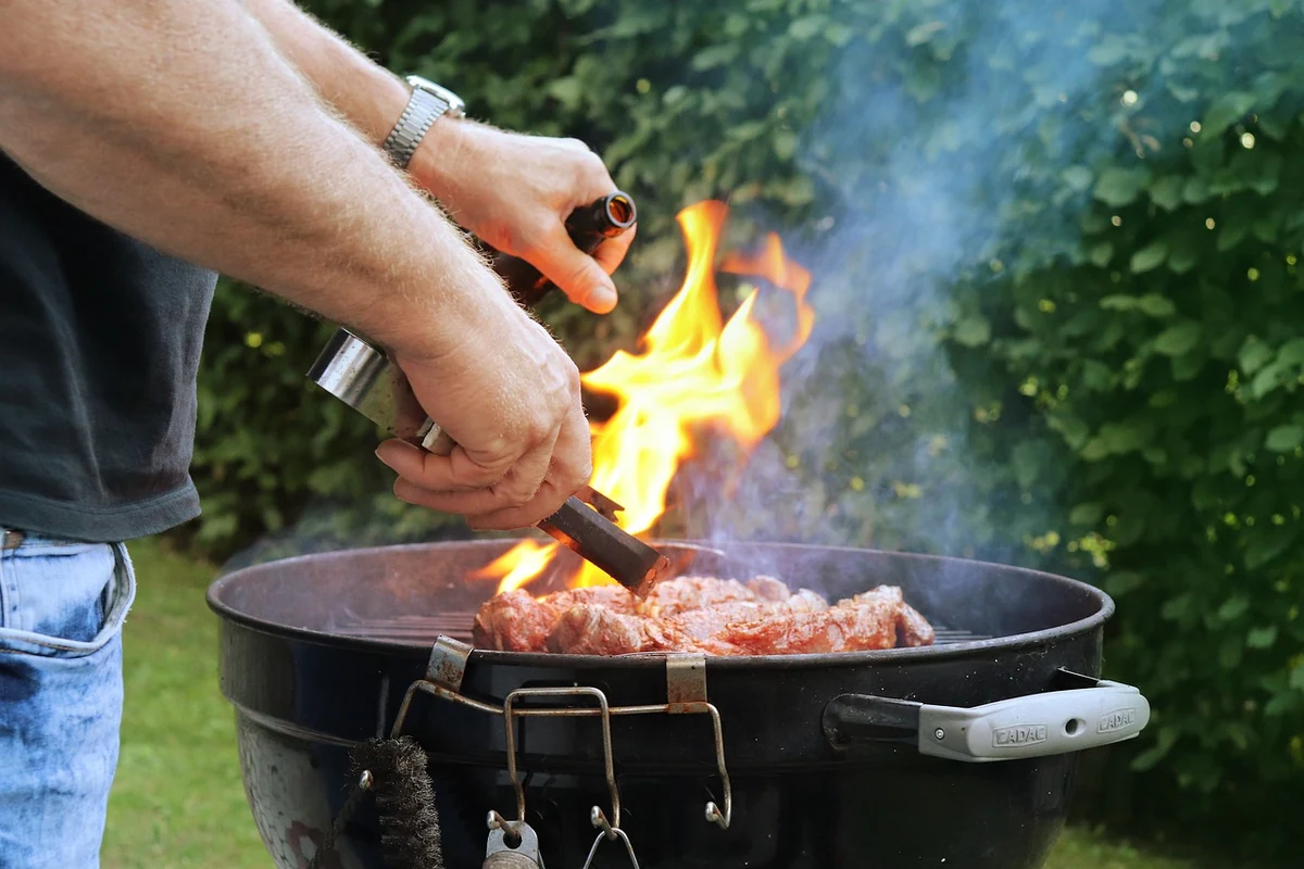 Dominando el arte del asado al carbón. Primer plano de las manos de un hombre cocinando carne en una clásica parrilla de carbón con llamas vivas.