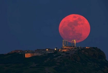 Luna de sangre de color rojo intenso sobre ruinas antiguas durante un eclipse lunar total.