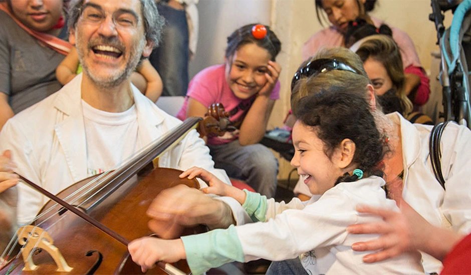 Aprender a sentir el ritmo y la música desde el inicio Clase de música donde un profesor y una niña ríen mientras tocan un instrumento de cuerda, representando la alegría de aprender el ritmo musical.