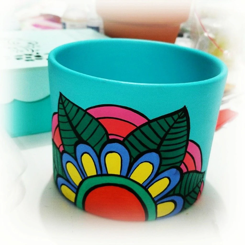 Diseño de mandalas para pintar macetas. Primer plano de una maceta de barro turquesa pintada a mano con un vibrante diseño de mandala floral.