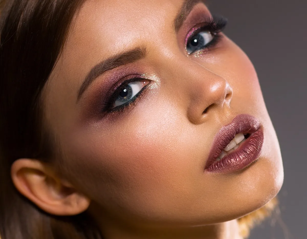 Primer plano de una mujer latina mostrando una tendencia de maquillaje 2025: ojos ahumados en tonos vino y piel luminosa.