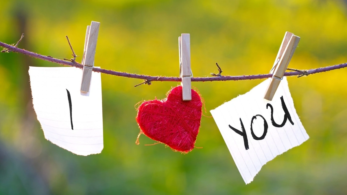 Papeles con las palabras “I” y “You” y un corazón rojo colgados en una cuerda con broches, sobre un fondo natural desenfocado