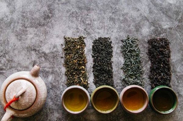 Diferentes tipos de té en hojas y en tazas junto a una tetera