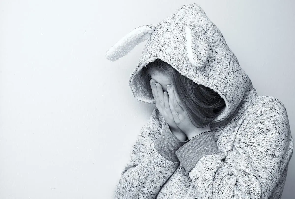Niña con sudadera cubriéndose la cara por miedo o angustia.