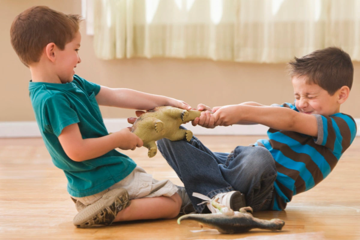 Dos niños peleando por un juguete en el suelo de una habitación.