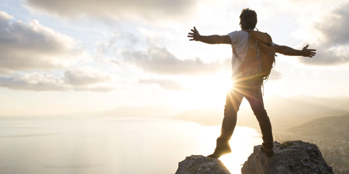 Persona alcanzando la cima de una montaña al amanecer, simbolizando motivación y superación personal.
