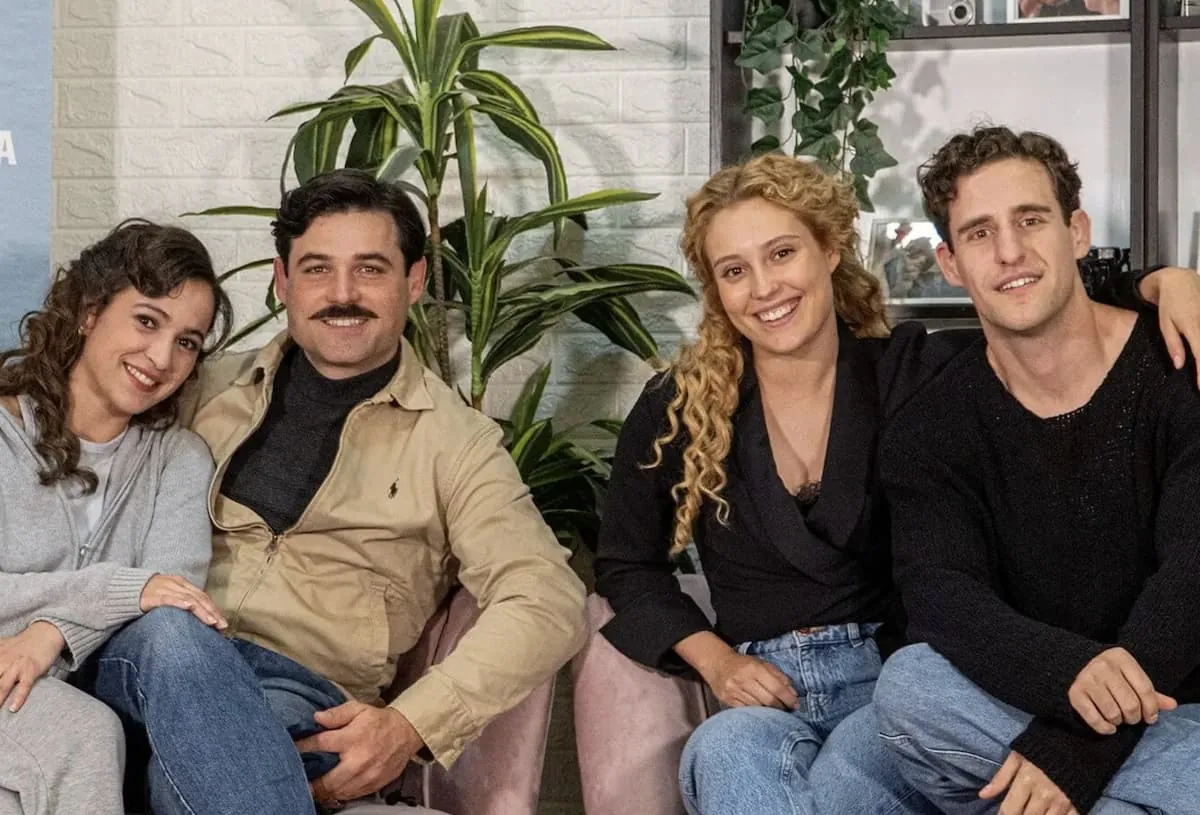 Los actores Ana Garcés (Jana) y Enrique Fortún (López Ruiz) de La Promesa, quienes son pareja en la vida real, sonriendo en una foto junto a otros compañeros de reparto.