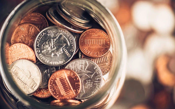 Frasco con monedas de dólar para representar el ahorro y los beneficios del coaching financiero.