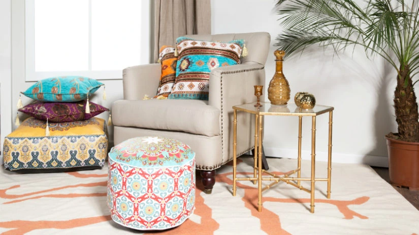 Rincón con sillón beige, puf estampado, almohadones de colores y mesa dorada junto a una palmera