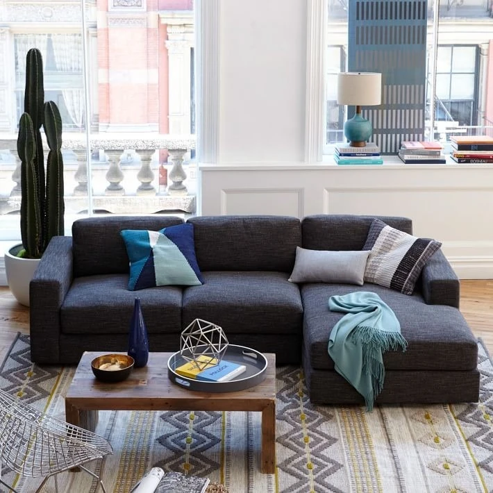 sala pequeña con sofá seccional gris oscuro y ventanal amplio con vista urbana