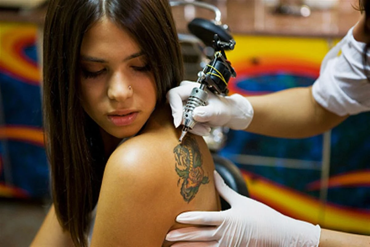 Tatuador con guantes blancos tatúa una rosa en el hombro de una joven