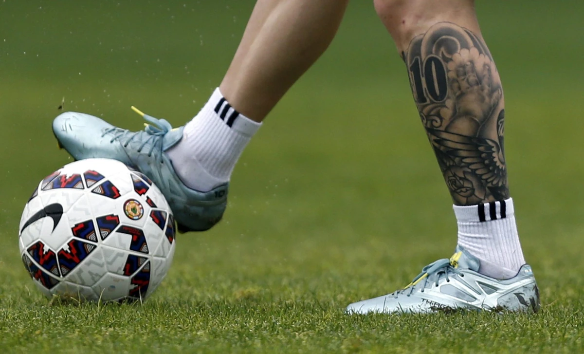 Pierna tatuada con el número 10 de un futbolista junto a un balón sobre el césped