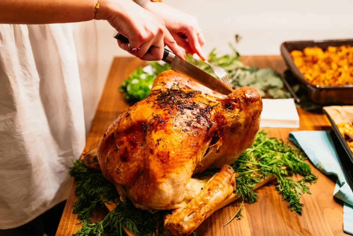 Pavo de Thanksgiving listo para servir durante la cena familiar. Persona cortando un pavo dorado de Thanksgiving sobre una mesa decorada con hierbas y guarniciones.