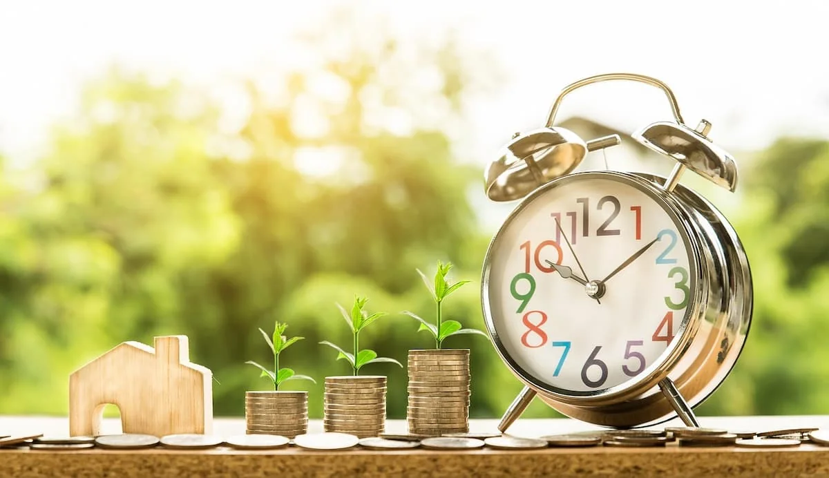 Reloj, monedas y plantas creciendo, simbolizando inversión y crecimiento del ahorro.