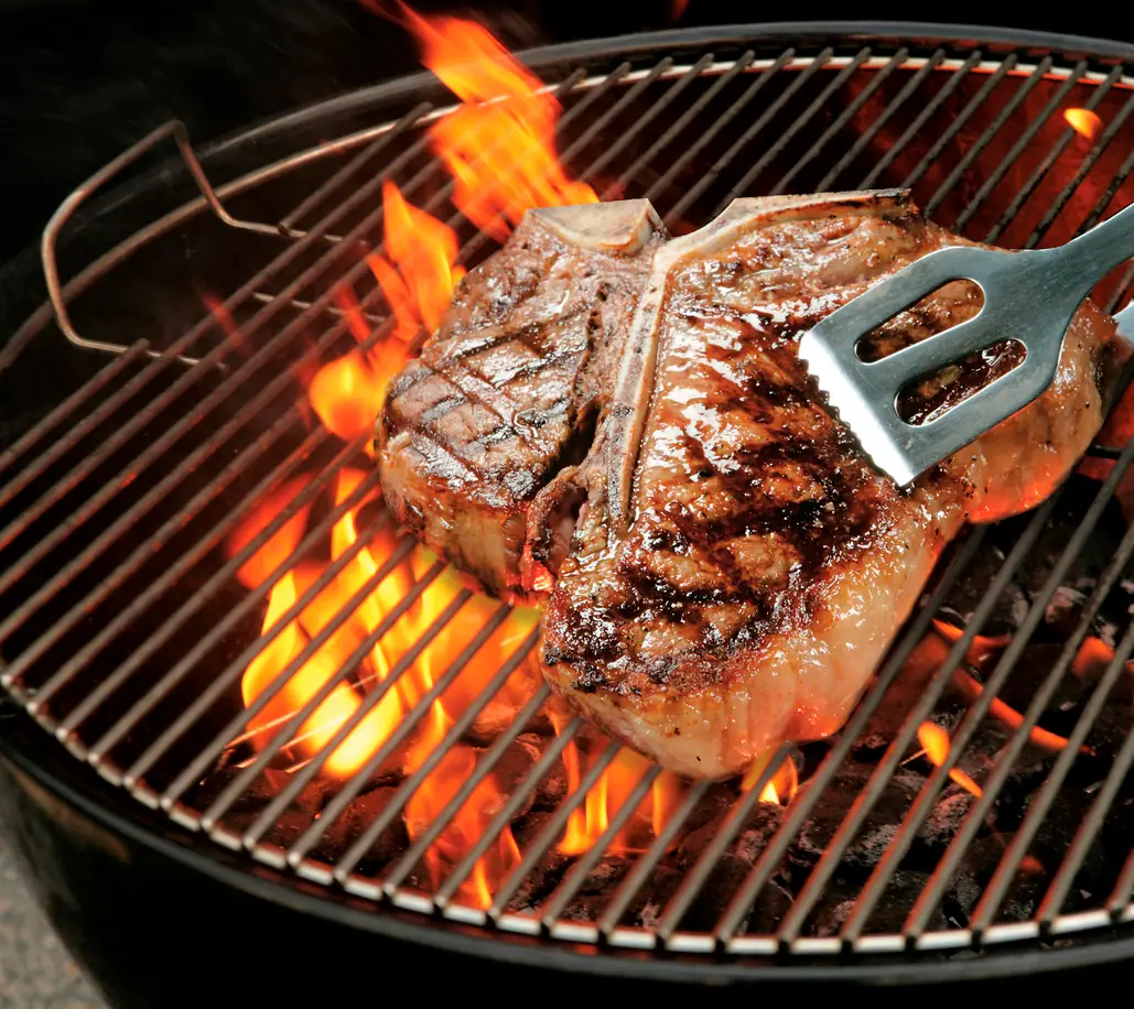 Parrilla: Cocción Rápida a Fuego Directo Corte de carne T-bone asándose en una parrilla con fuego alto para mostrar la diferencia con la barbacoa.