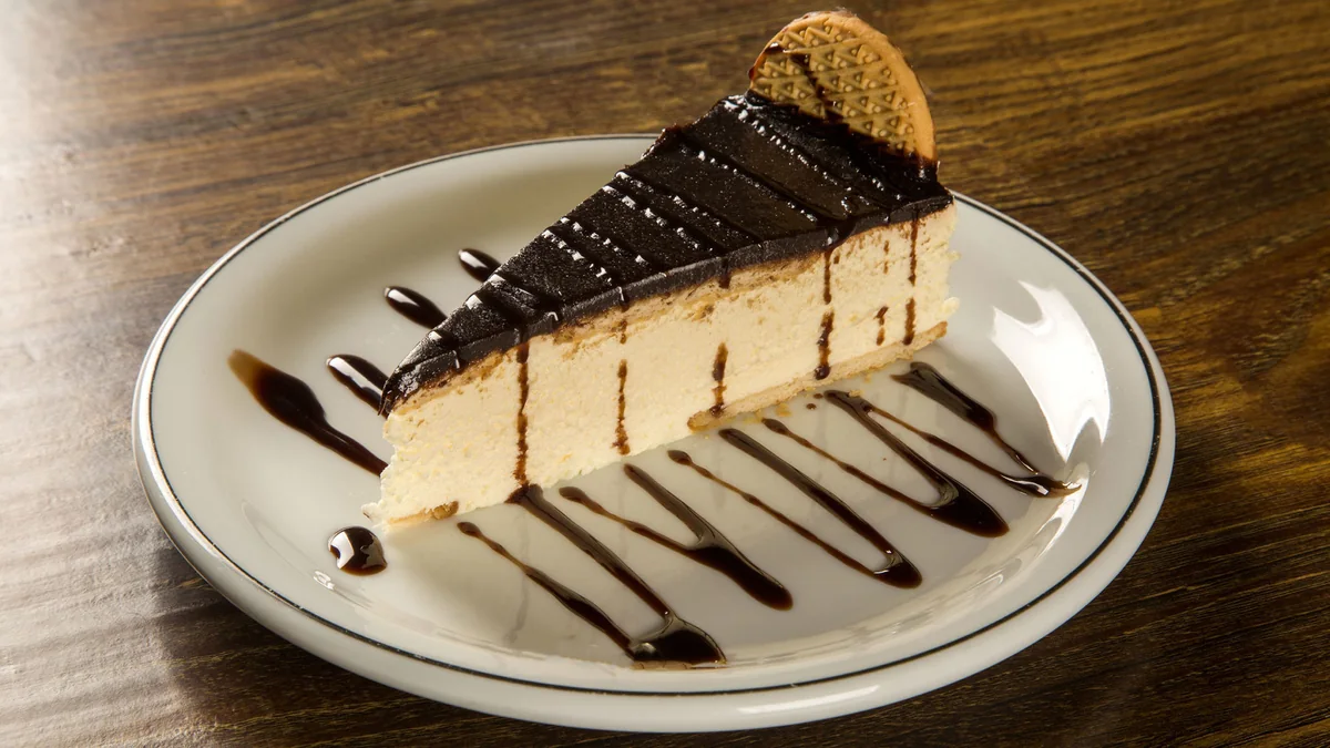 Porción de tarta de queso con cobertura de chocolate, galleta y hilos de salsa