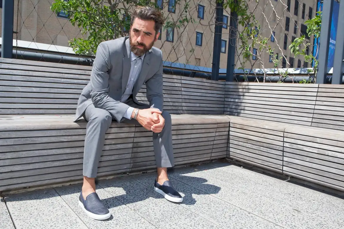 hombre sentado con traje gris y slip-on azules en banco urbano