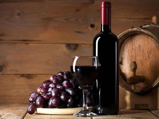 Botella y copa de vino tinto con uvas frescas y barrica de madera