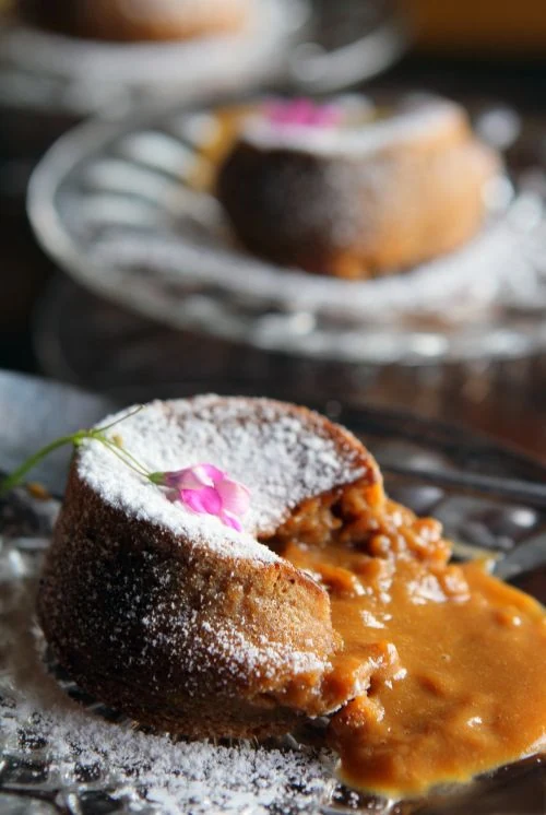 El Secreto para un Centro Líquido Perfecto. Primer plano de un volcán de dulce de leche casero, con el centro líquido de cajeta fluyendo del bizcocho y espolvoreado con azúcar glass.