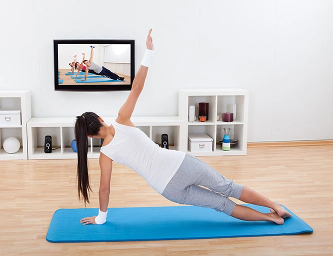 Clases de yoga y pilates online en YouTube Mujer practicando pilates en casa frente a la televisión con clases online, ejemplo de tendencia fitness en YouTube